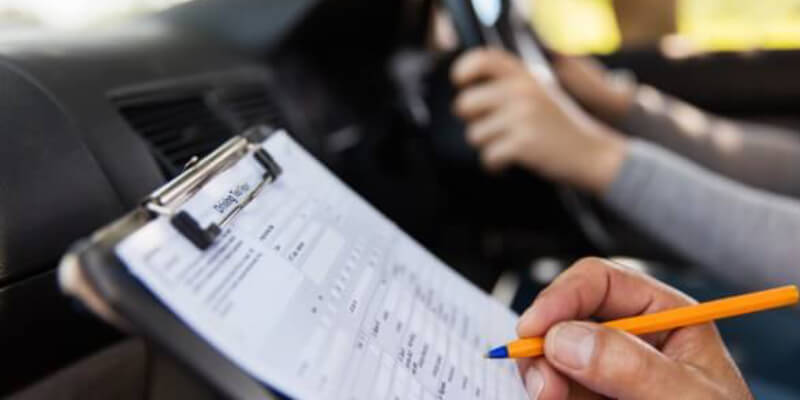 Examiner's hand with pen marking driving test sheet