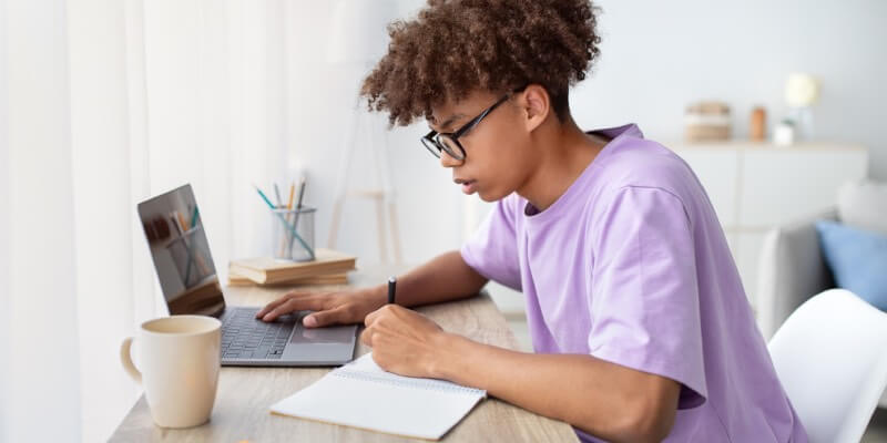 Boy writing with one hand and typing on computer with the other